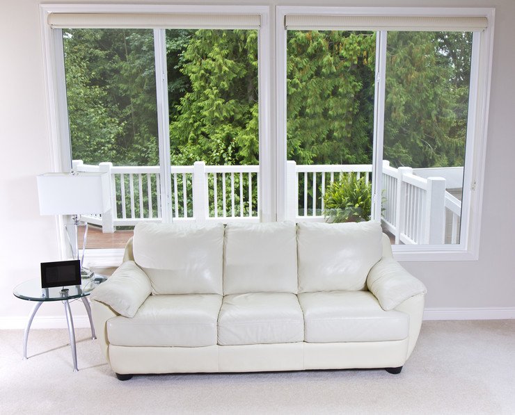 Остекленная комната с мягким диваном белого цвета и журнальным столиком в загородном доме