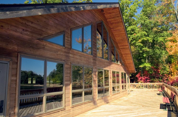 Остекленный панорамными оконными системами деревянный коттедж, огражденная терраса, скамейки