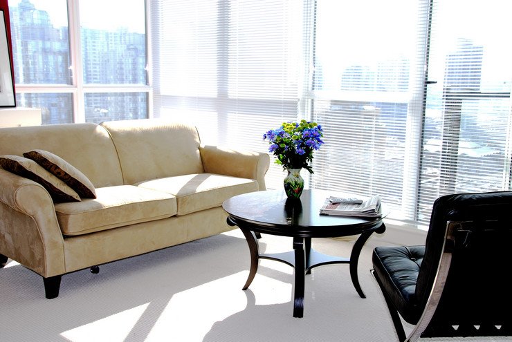 Панорамные оконные блоки в офисном помещении, мягкий стул, диван с подушками, ваза с цветами на круглом столике