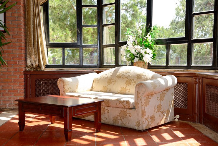 Остекленная нестандартными евроокнами терасса в загородном доме, мягкий диван, журнальный столик, цветы