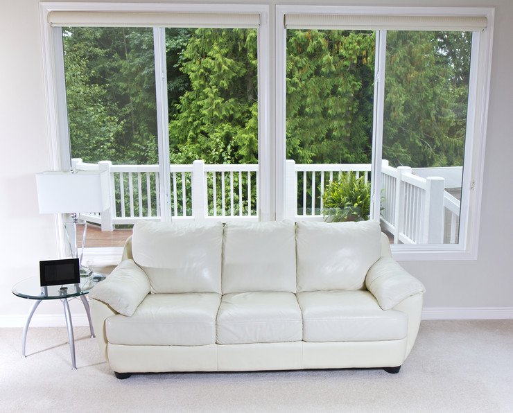 Большие оконные системы в комнате с видом на террасу, мягкий белый диван и круглый журнальный столик