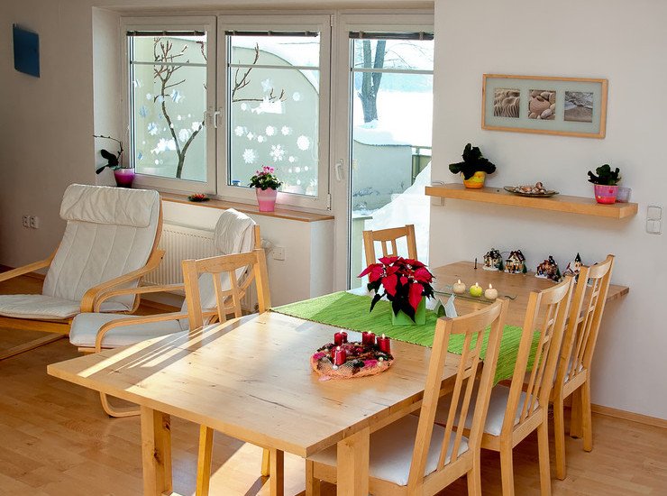 Остекление гостиной, деревянные столы, стулья, мягкие кресла, полка с цветами в небольших вазонах